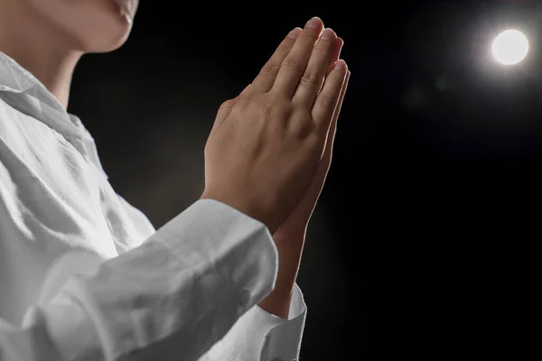 Woman holding hands clasped while praying on black background, closeup