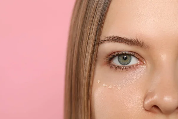 Young woman with cream around eye on pink background, closeup. Space for text