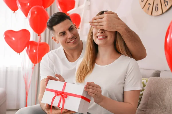 男人在装饰有心形气球的房间里送给女朋友礼物 情人节庆祝活动 — 图库照片