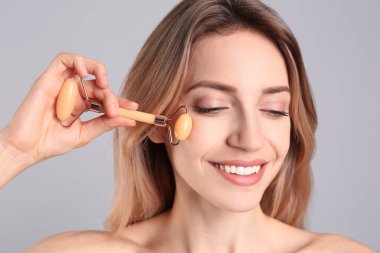 Genç bir kadın açık gri arka planda doğal yeşil yüz silindiri kullanıyor.