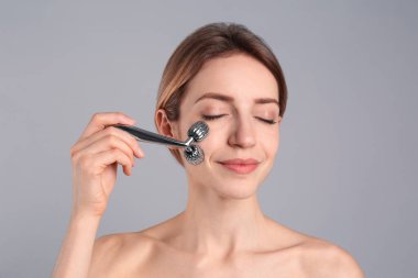 Açık gri arka planda metal yüz silindiri kullanan genç bir kadın