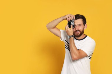 Kameralı adam sarı arkaplanda fotoğraf çekiyor, mesaj için yer var. İlginç bir hobi.