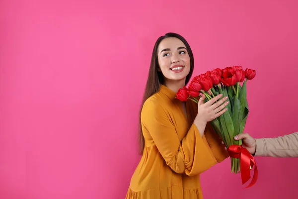 ピンクの背景の男性から赤いチューリップの花束を受け取った幸せな女性 テキストのためのスペース 3月8日 — ストック写真