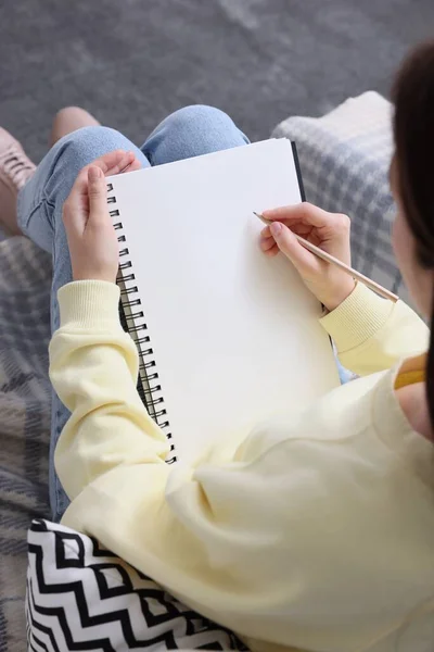 Young woman drawing in sketchbook indoors, closeup