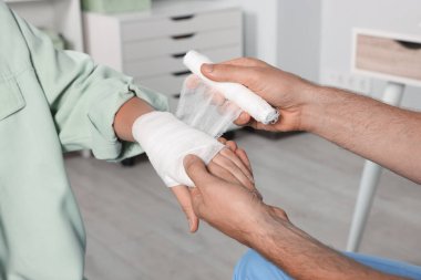 Doktor hastanedeki hastanın eline bandaj uyguluyor.