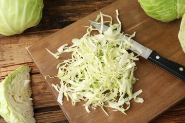 Chopped ripe cabbage and knife on wooden board, closeup