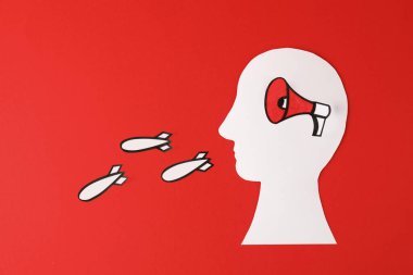 Paper human cutout with megaphone in head and bombs flying out of mouth on red background, flat lay. Hybrid war concept clipart