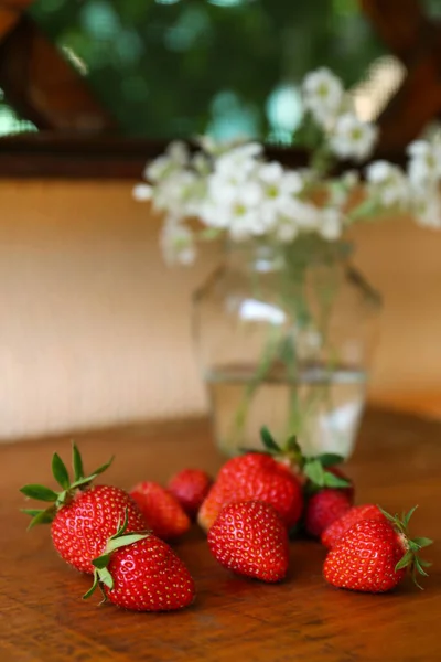 Fresh ripe strawberries and bouquet of beautiful flowers on wooden table, closeup