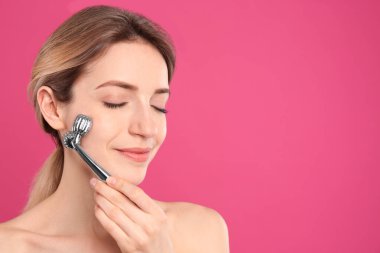 Pembe arka planda metal yüz silindiri kullanan genç kadın, metin için boşluk
