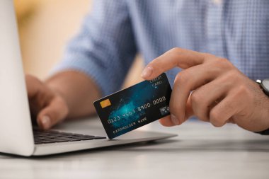Bilgisayarı ve kredi kartını kapalı bir masada online ödeme için kullanan bir adam, yakın plan.