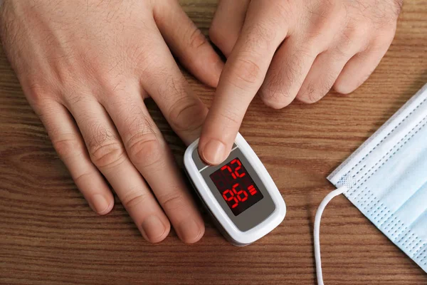 Mann Mit Pulsoximeter Zur Sauerstoffmessung Holztisch Mit Medizinischer Maske Draufsicht — Stockfoto