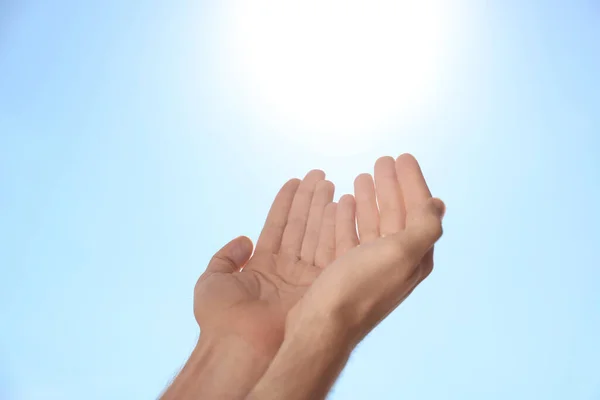 Man reaching hands to blue sky outdoors on sunny day, closeup