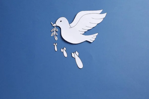 White paper dove with olive branch and bombs on blue background, flat lay