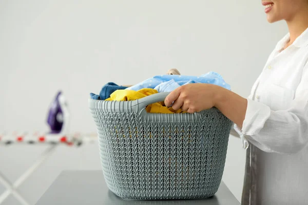 Woman with basket full of clean laundry at grey table indoors, closeup