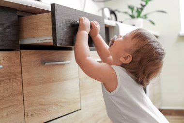 Little child exploring drawer indoors. Dangerous situation