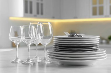 Different clean dishware, cutlery and glasses on white marble table in kitchen