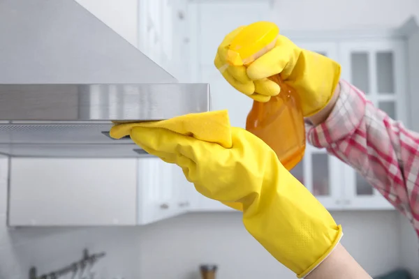 Woman cleaning kitchen hood with rag and detergent indoors, closeup