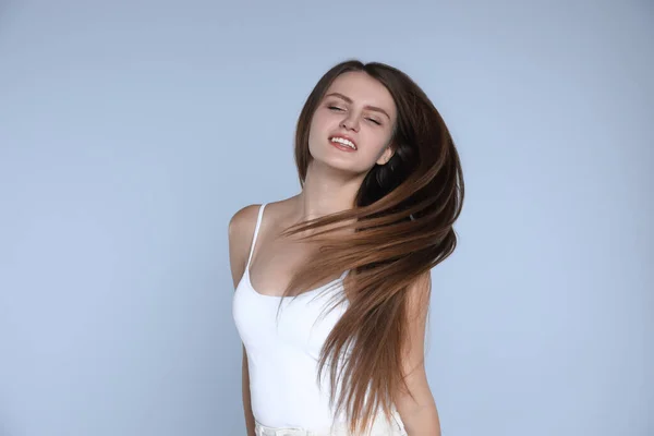 Young woman with strong healthy hair on light blue background