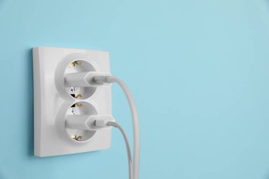 Açık mavi duvardaki güç prizlerine bağlı şarj adaptörleri, metin için boşluk. Elektrik arzı