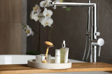 Bath tray with natural face roller and cosmetic products on tub