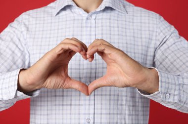 Kırmızı arka planda elleri olan adam kalp yapıyor, yakın plan.