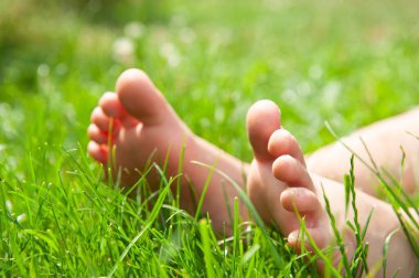 Yeşil çimenlerde çıplak ayakla oturan çocuk, yakın plan.