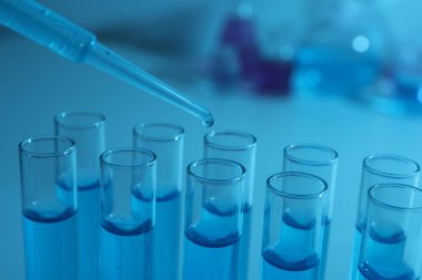 Test tüpüne mavi sıvı damlatılıyor, yakın plan. Laboratuvar analizi