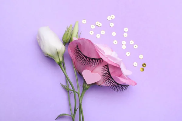 Flower with false eyelashes and pink paper heart as beautiful face on violet background, flat lay