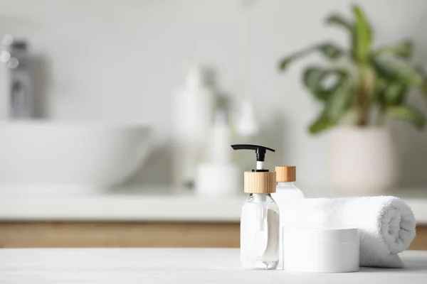 Different personal care products and rolled towel on white wooden table in bathroom. Space for text