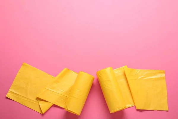 Rolls of yellow garbage bags on pink background, flat lay. Space for text