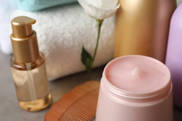 Different hair products, flower and wooden comb on grey table, closeup