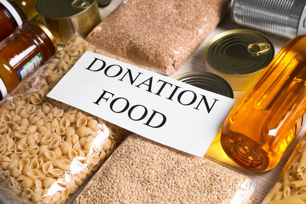 Card with words Donation Food and different products on white table, closeup