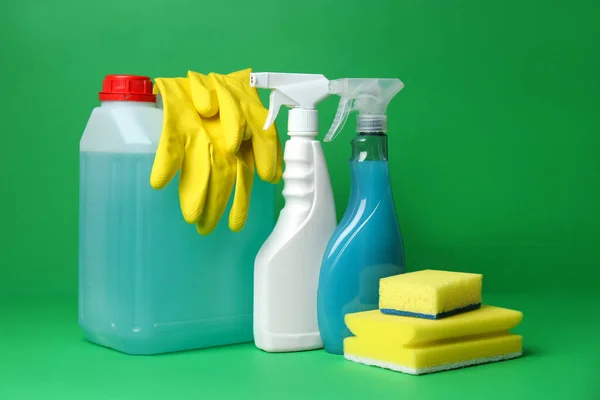 Different cleaning supplies and tools on green background