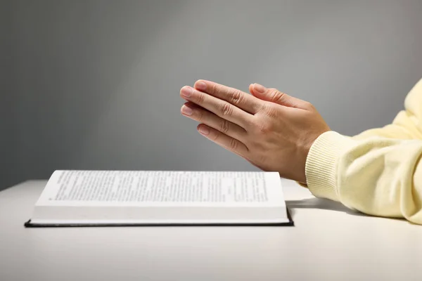 Vrouw Biddend Bijbel Aan Witte Tafel Tegen Grijze Achtergrond Close — Stockfoto