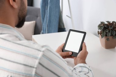 Man using e-book reader at white table indoors, closeup