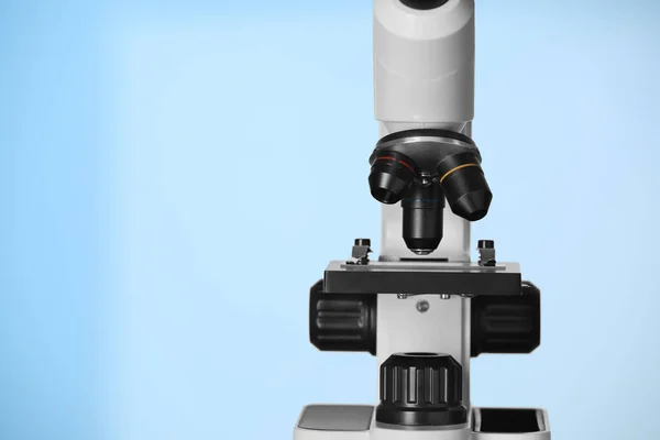 Modern microscope on light blue background, closeup. Space for text