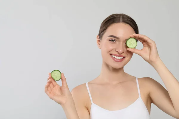 Young woman with cucumber slices on white background, space for text. Eye skin care