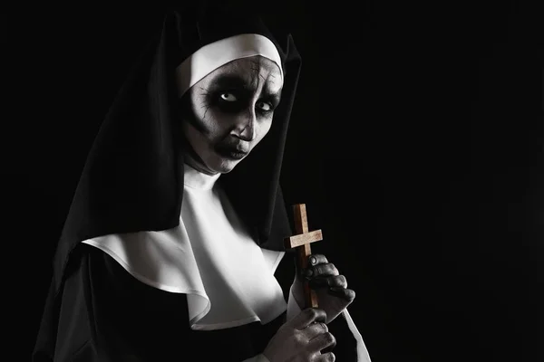 Scary devilish nun with cross on black background, space for text. Halloween party look