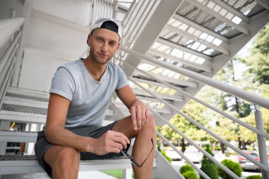 Dışarıda merdivenlerde oturan şık şapkalı yakışıklı genç adam.