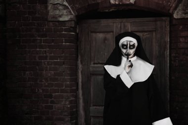 Kırmızı tuğla duvarın yanında korkunç bir rahibenin portresi. Cadılar Bayramı partisi görünüşü