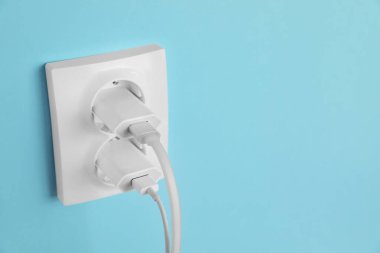 Açık mavi duvardaki güç prizlerine bağlı şarj adaptörleri, metin için boşluk. Elektrik arzı