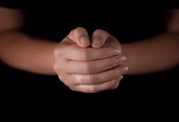 Woman holding hands clasped while praying against black background, closeup