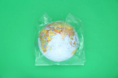 Globe in plastic bag on light green background, top view. Environmental conservation