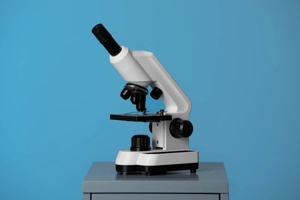 Modern microscope on table against blue background. Medical equipment