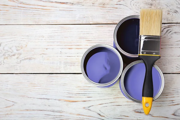 Cans with violet paints and brush on white wooden background, top view. Space for text