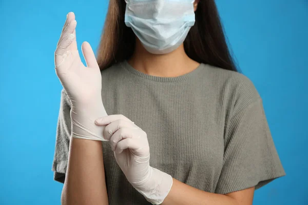 Kvinna Skyddande Ansiktsmask Sätta Medicinska Handskar Mot Blå Bakgrund Närbild — Stockfoto