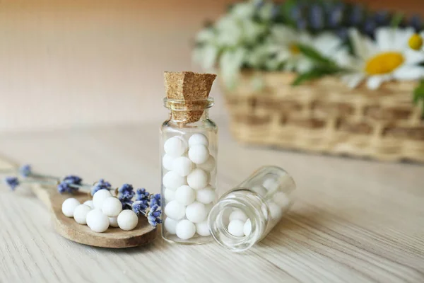 Bottles with homeopathic remedy and flowers on wooden table, closeup