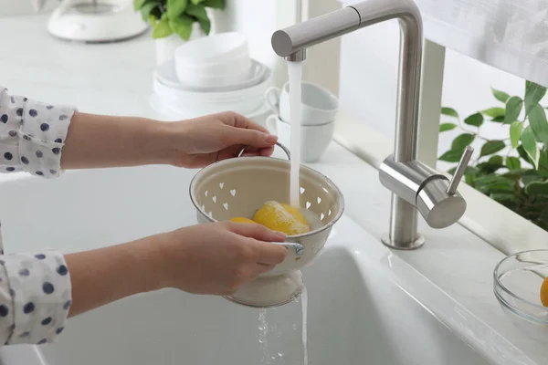 Woman washing fresh ripe lemons under tap water in kitchen, closeup