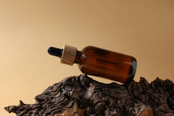 Bottle of essential oil on tree bark against dark beige background