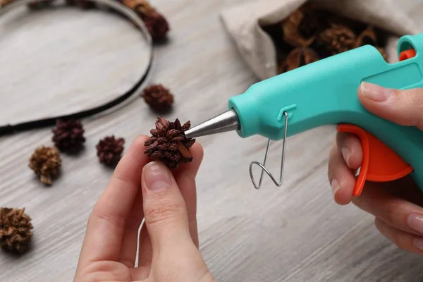 Woman with hot glue gun making craft at wooden table, closeup